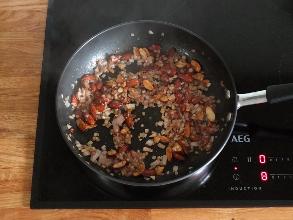 Image of chopped shallots and raw almonds cooking in a frying pan.