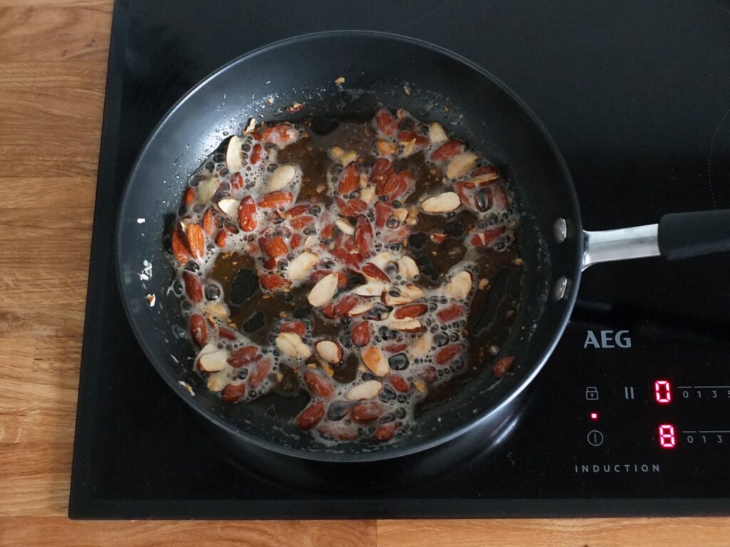 Image of halved raw almonds frying in butter in a frying pan.